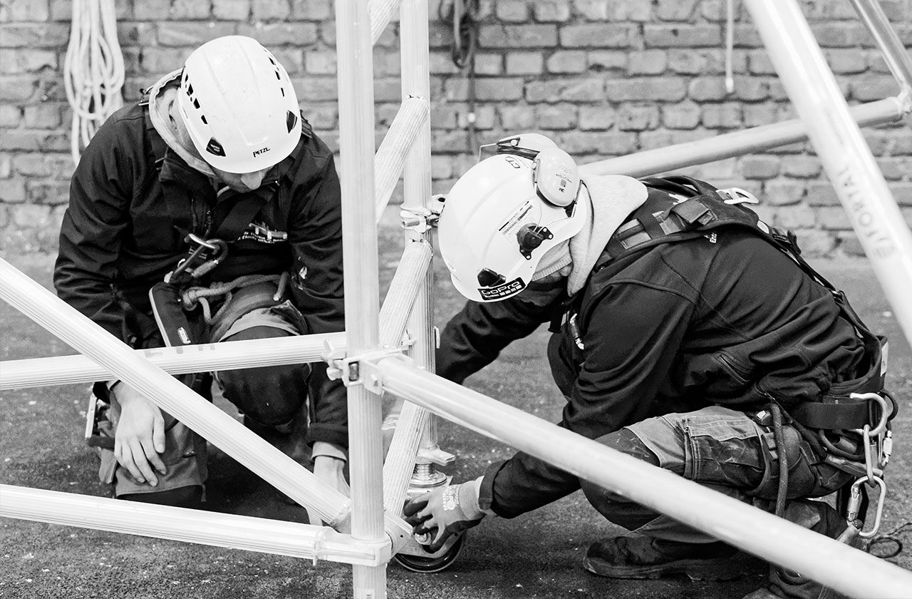 deux travailleurs avec casques et harnais assemblant une structure métallique